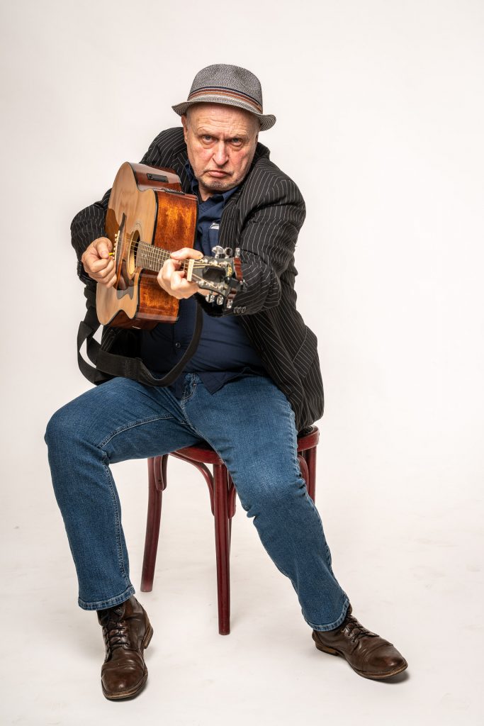 Heinz Klever mit Gitarre auf einem Stuhl